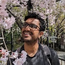 A photo of Mahesh Makani, under a cherry blossom tree. He is smiling and looking towards the top left of the image.